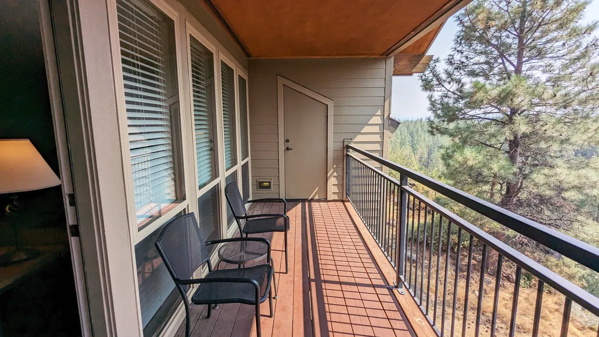 This image shows two black chairs set on a private balcony, overlooking lush trees and the serene landscape beyond. The balcony's door to the interior is open, inviting one to step outside and soak in the forest views. The tranquil scene is perfect for enjoying morning coffee, reading, or unwinding with a friend.