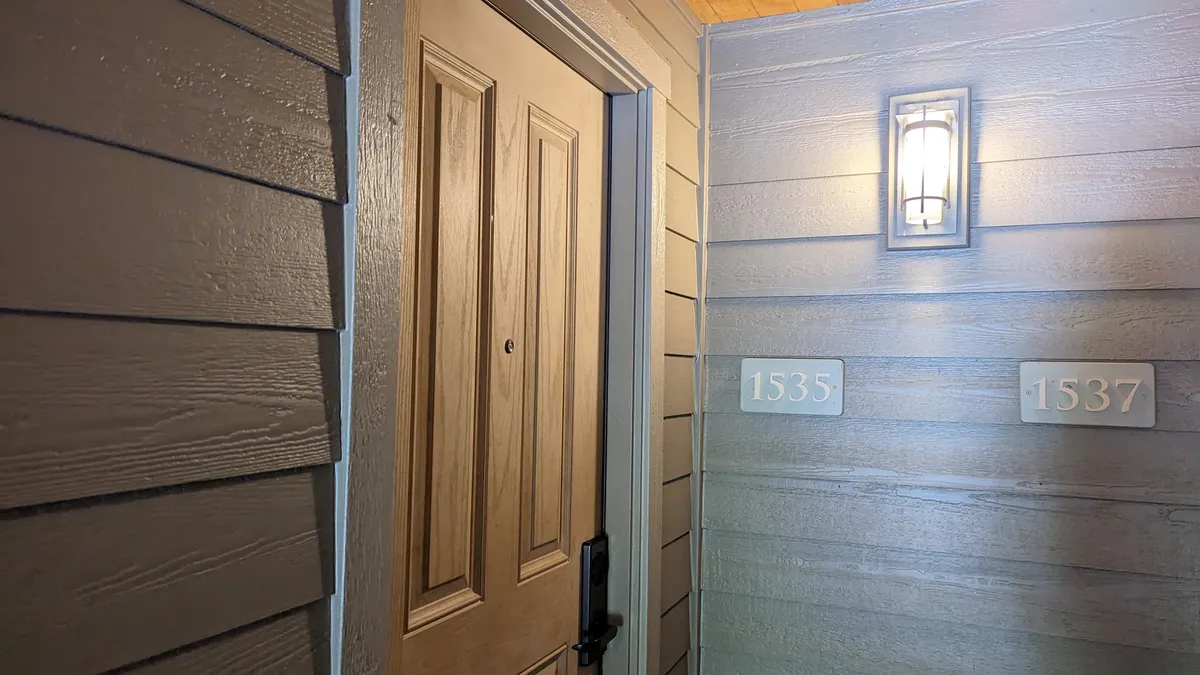 A close-up of the property's front door, with a wooden finish, address numbers, and a glowing light fixture. The image conveys a sense of arrival and anticipation, inviting guests to step inside and discover what awaits.