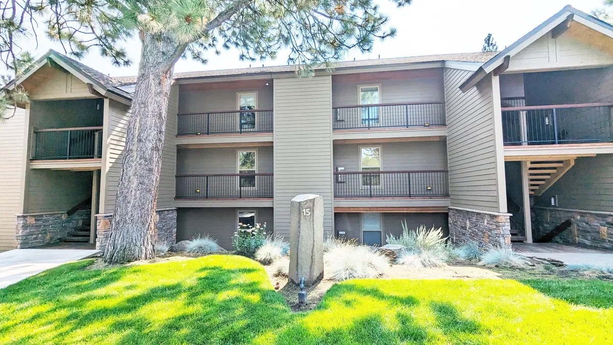 This image captures the exterior of the resort, featuring a three-story building, a lush green lawn, and a decorative stone sign. The scene conveys a welcoming atmosphere, showcasing the property's inviting grounds and its connection to the outdoors.