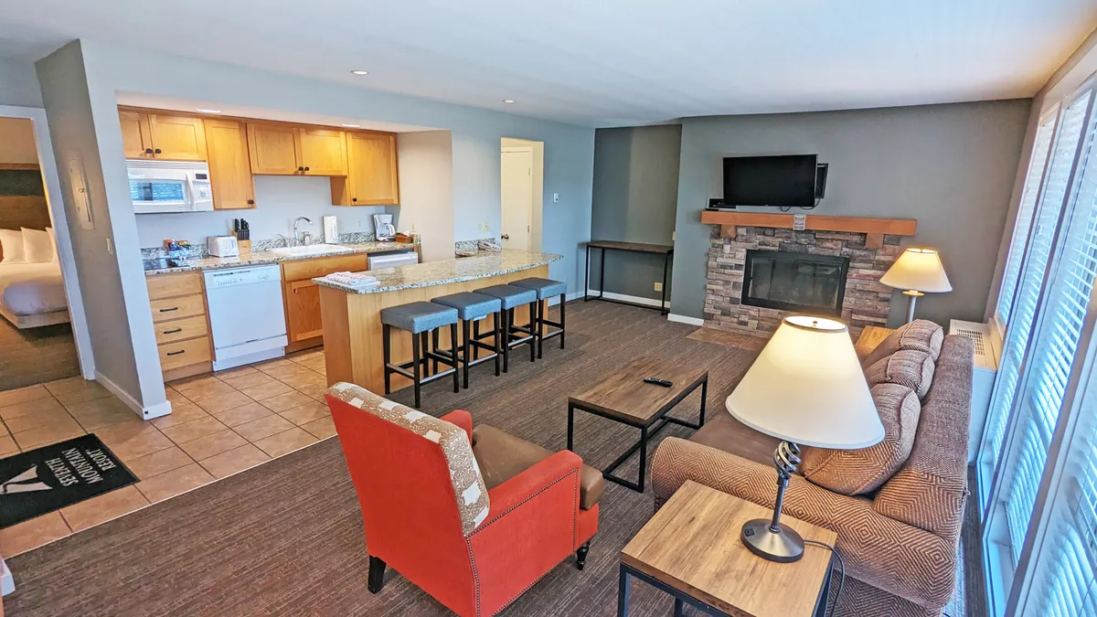 A cozy living space featuring a sofa, kitchen island, fireplace, television, and warm lighting. The arrangement encourages relaxation, socializing, and group activities like game nights or planning the next day's fun.