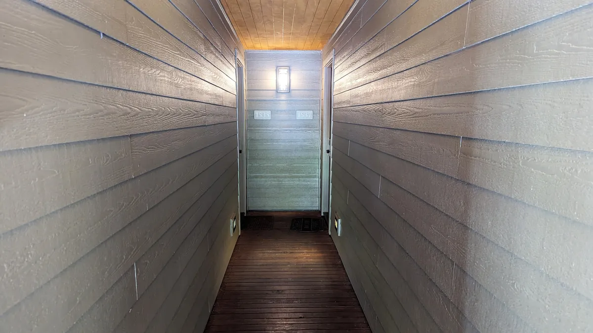 A welcoming hallway with wooden flooring, horizontal plank walls, and bright light fixtures. The image captures the inviting entryway leading to the rest of the property, with doorways visible and a sense of movement towards shared living spaces.