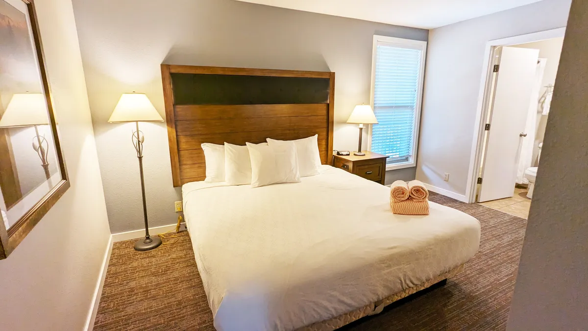 A serene bedroom scene featuring a plush king bed dressed in crisp white bedding, a wooden headboard, and matching nightstands with warm lamps. Soft natural light filters into the room, creating a peaceful and intimate atmosphere, ideal for relaxation and restful sleep.