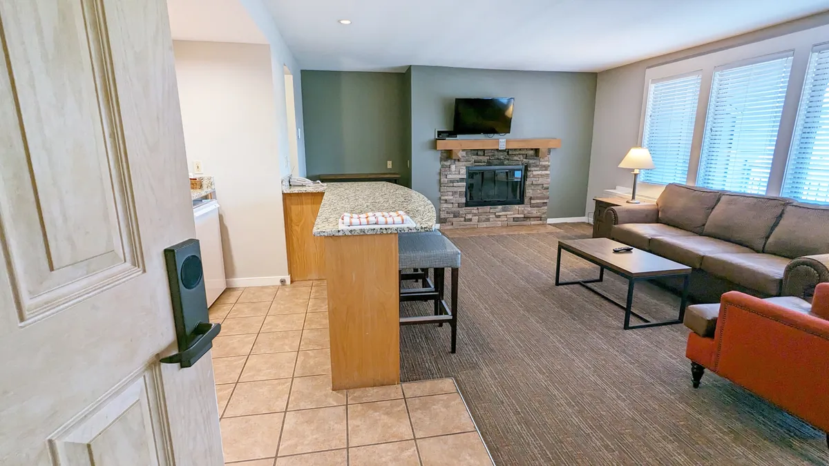 A cozy view focused on the living area with a plush sofa facing a warm fireplace. The kitchen counter is visible in the background, tying together the living and dining zones. Sunlight streams in through a window, enhancing the inviting mood and highlighting the space where guests can relax, socialize, and unwind after outdoor adventures.